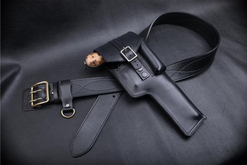displayed with matching belt, buckle closure, and handgun on black leather surface