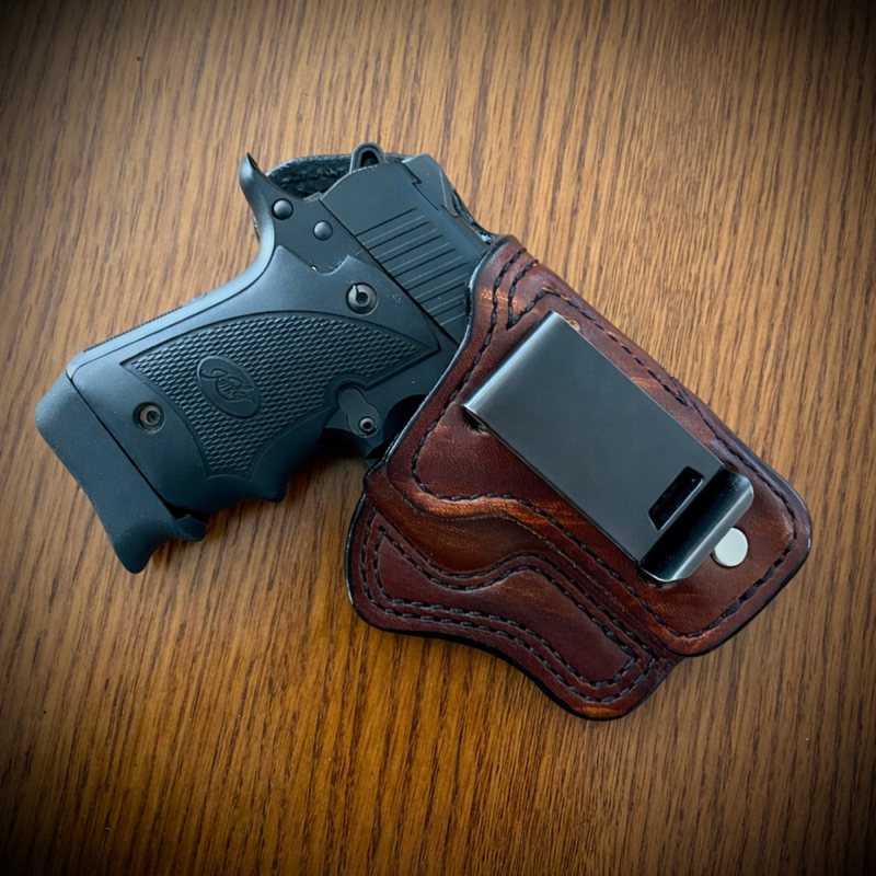 Brown leather IWB holster with zero cant and metal belt clip on wooden surface
