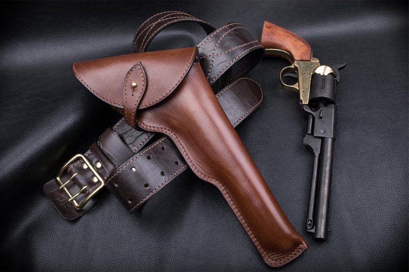 displayed with matching leather belt and long barrel revolver on black leather surface