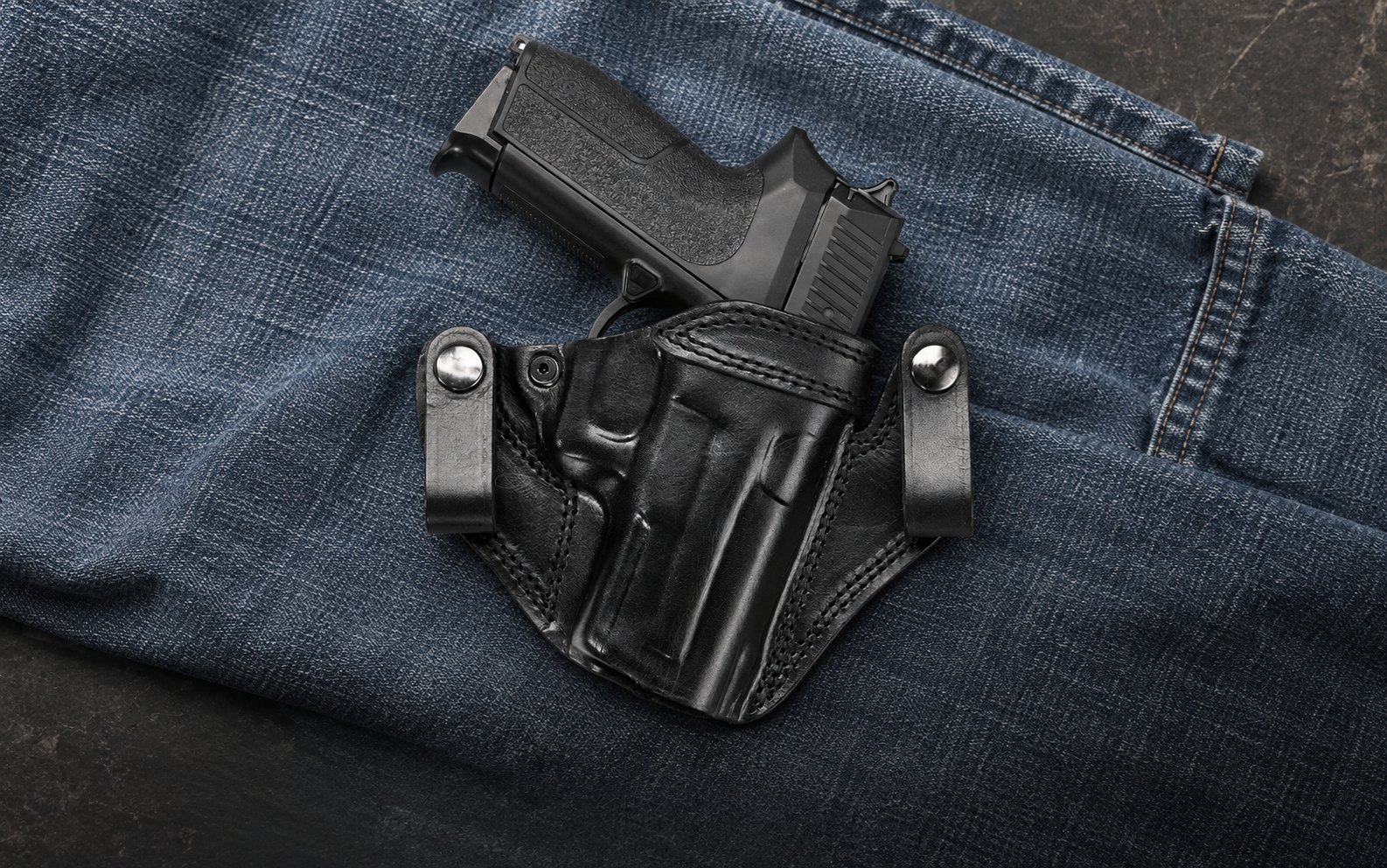 Schwarzes IWB-Lederholster mit zwei Druckknopfschlaufen auf blauem Denim